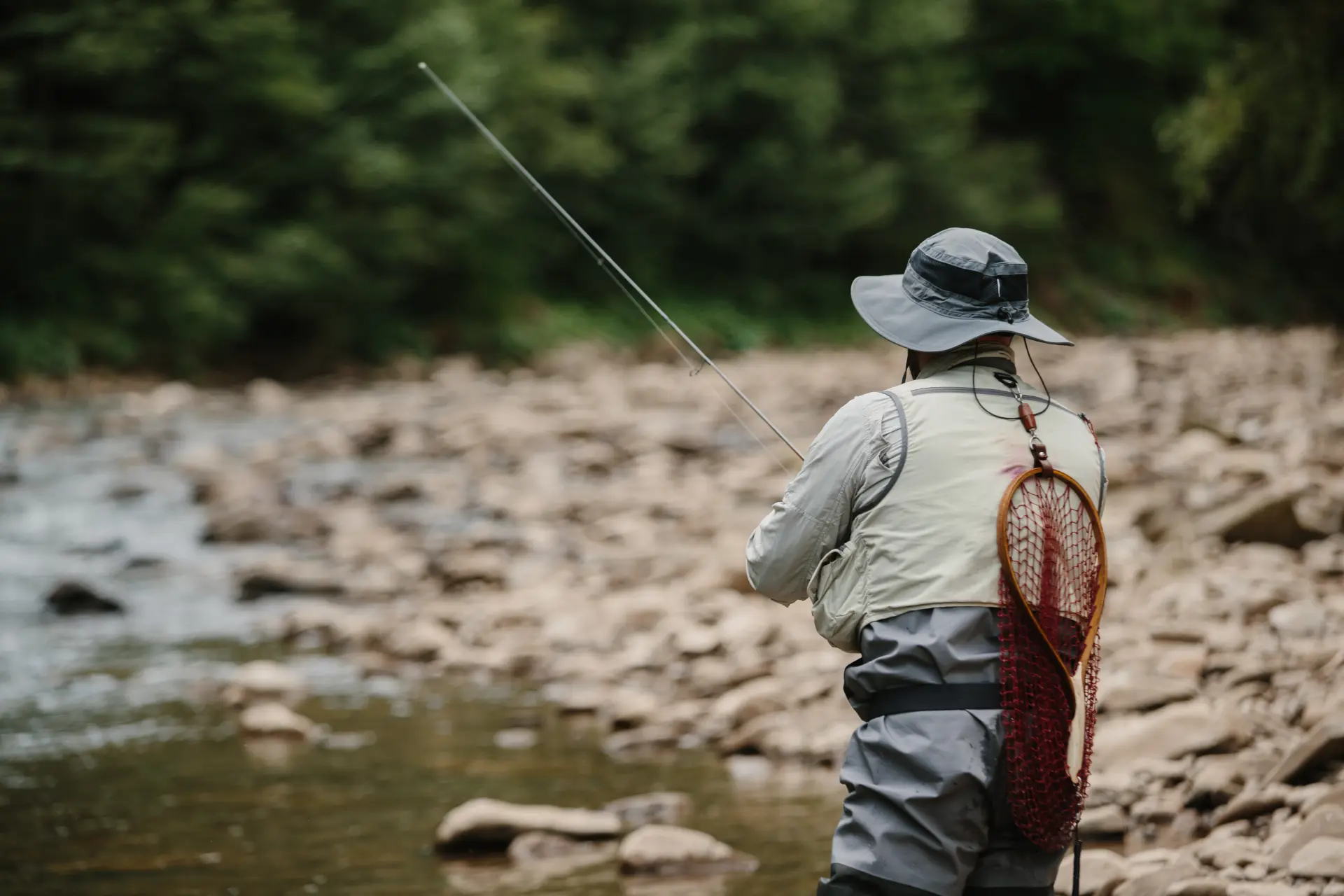Fly angler carrying a landing net beside a rocky river